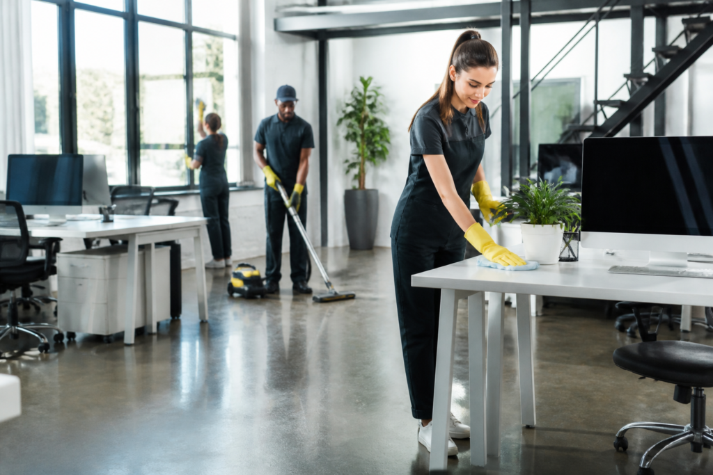 office cleaning services — Professional cleaner disinfecting a modern office desk with supplies in hand